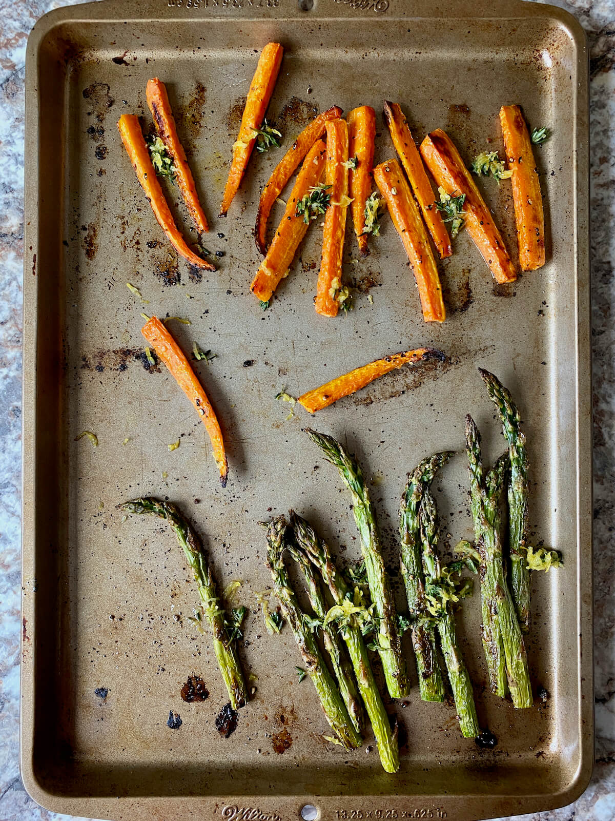 Roasted asparagus and carrots garnished with lemon and thyme on a rimmed baking sheet.