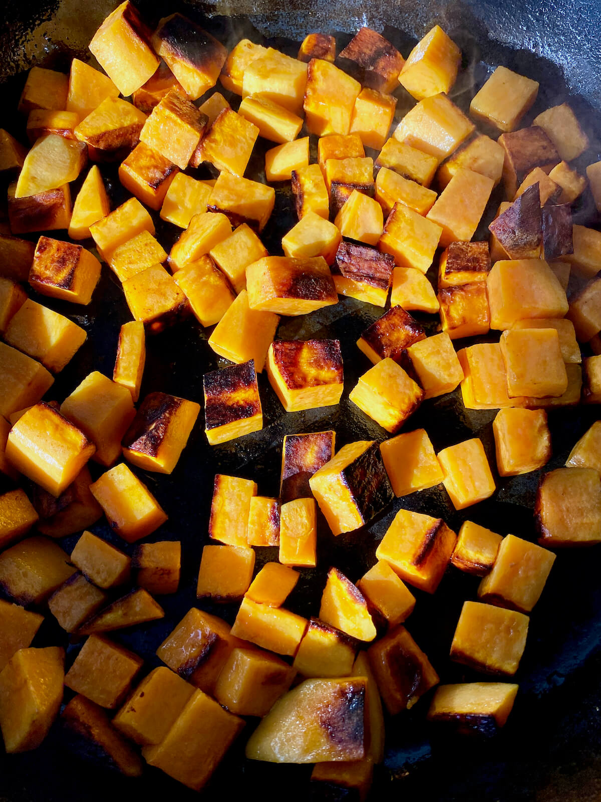 Browned sweet potatoes cooking in a cast iron skillet.