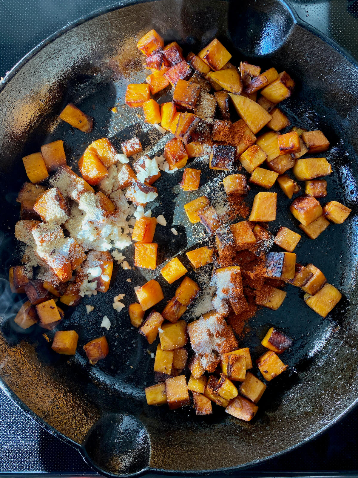Cooked sweet potatoes in a cast iron skillet with seasonings sprinkled over the top of them.