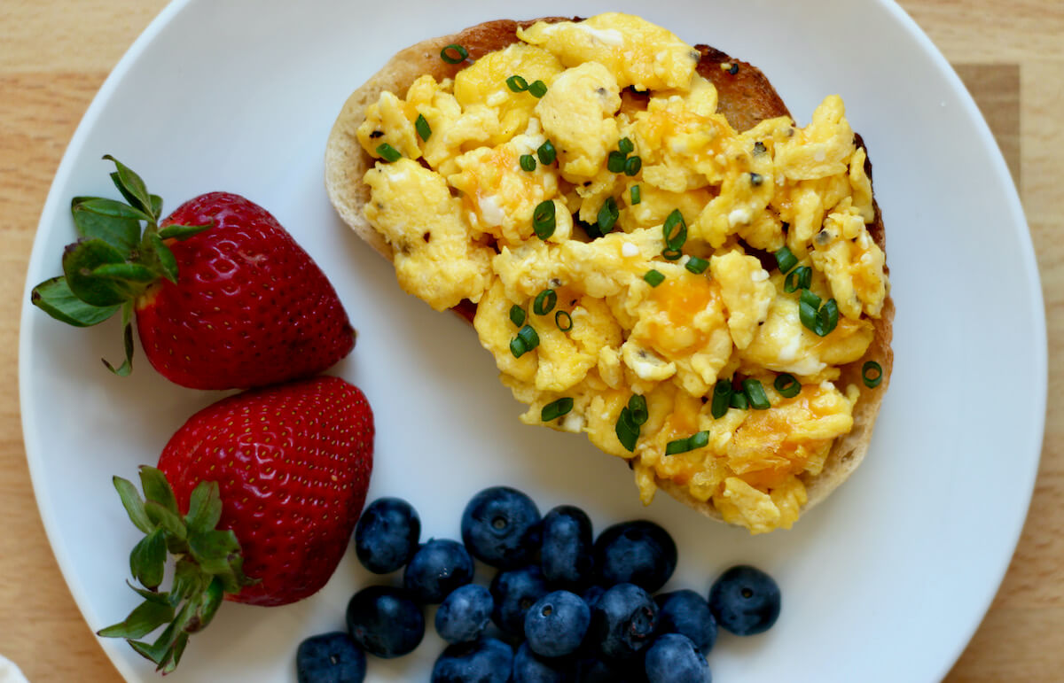 Scrambled eggs on toast on a white plate with strawberries and blueberries.
