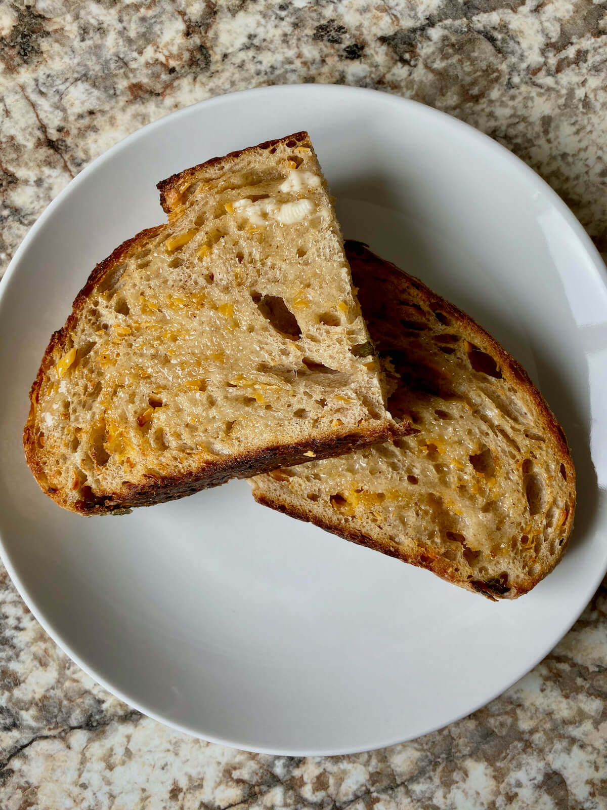 A piece of buttered sourdough toast cut in half on a small white plate.