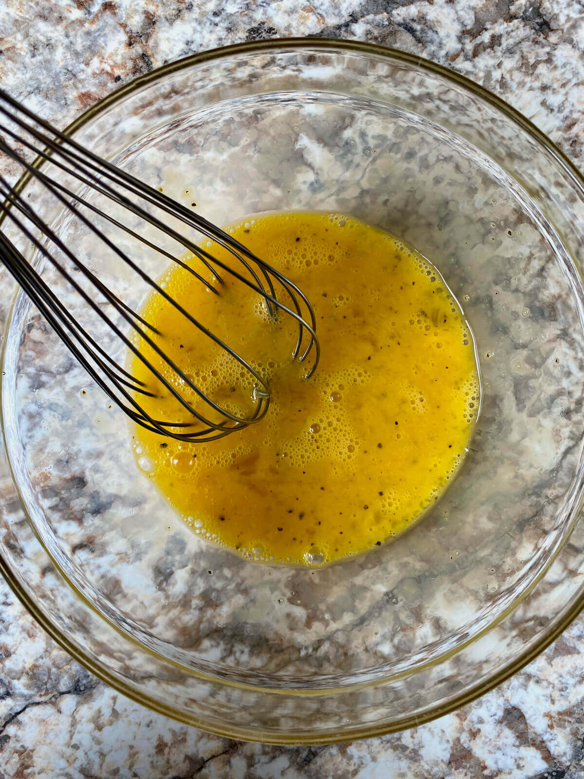 Two beaten eggs in a glass mixing bowl with a whisk sticking out.