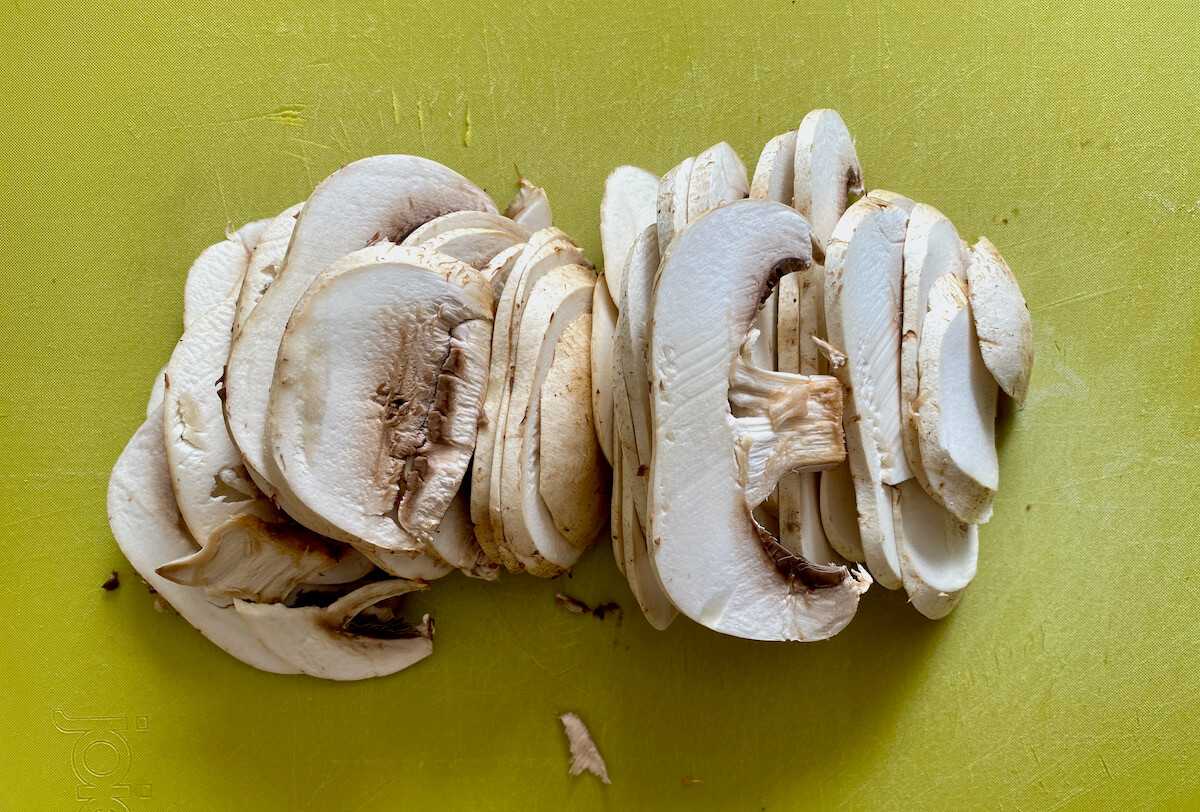 Sliced button mushrooms on a green cutting board.