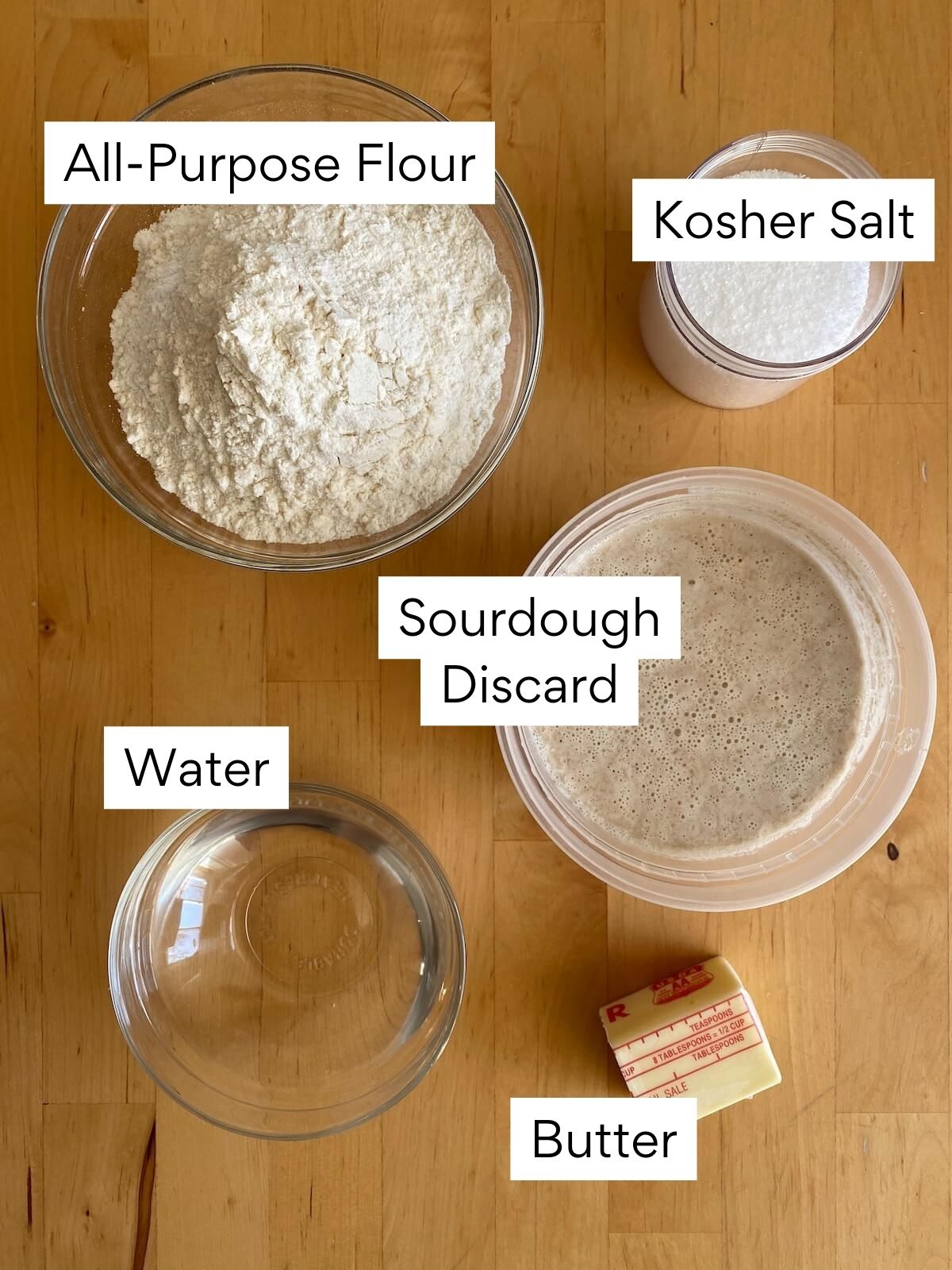 The ingredients to make sourdough discard tortillas. Each ingredient is labeled with text. They include all-purpose flour, kosher salt, sourdough discard, water, and butter.