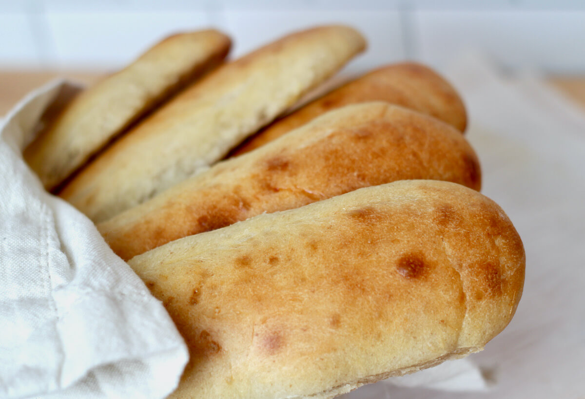 A basket of sourdough hoagie rolls wrapped in a white cloth napkin.