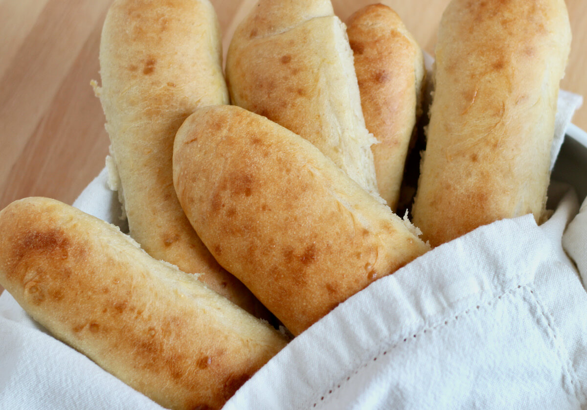 Six sourdough hoagie rolls wrapped in a white cloth napkin in a bowl.