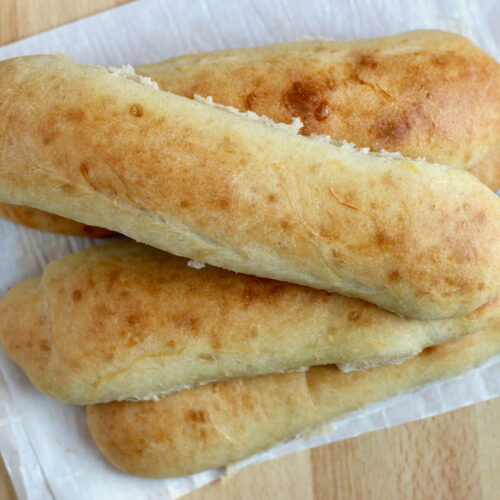 A stack of five sourdough hoagie rolls on a sheet of parchment paper.