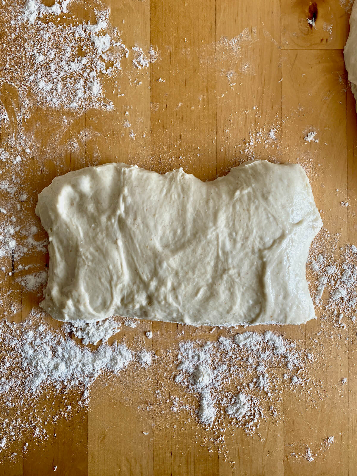 A piece of dough pulled into the shape of a rectangle on a floured work surface.