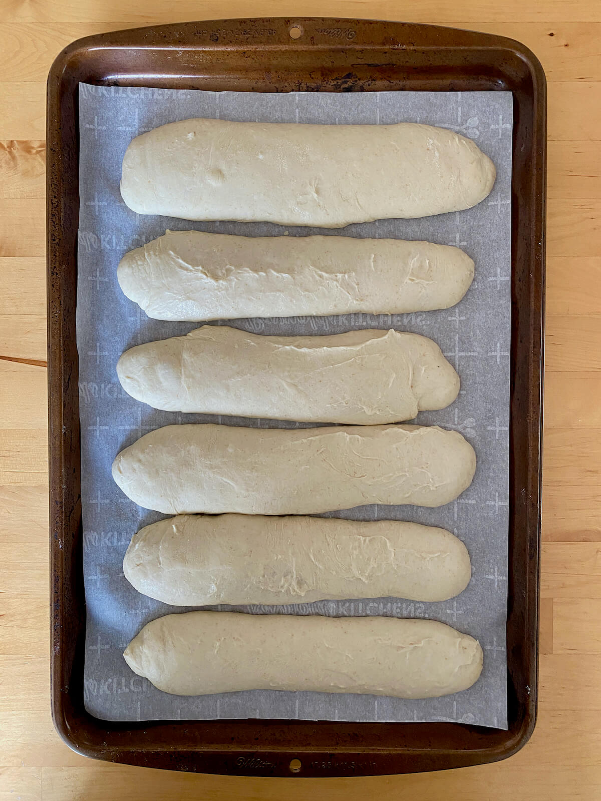 Six sourdough discard hoagie rolls on a parchment-lined baking sheet after proofing and before being baked.