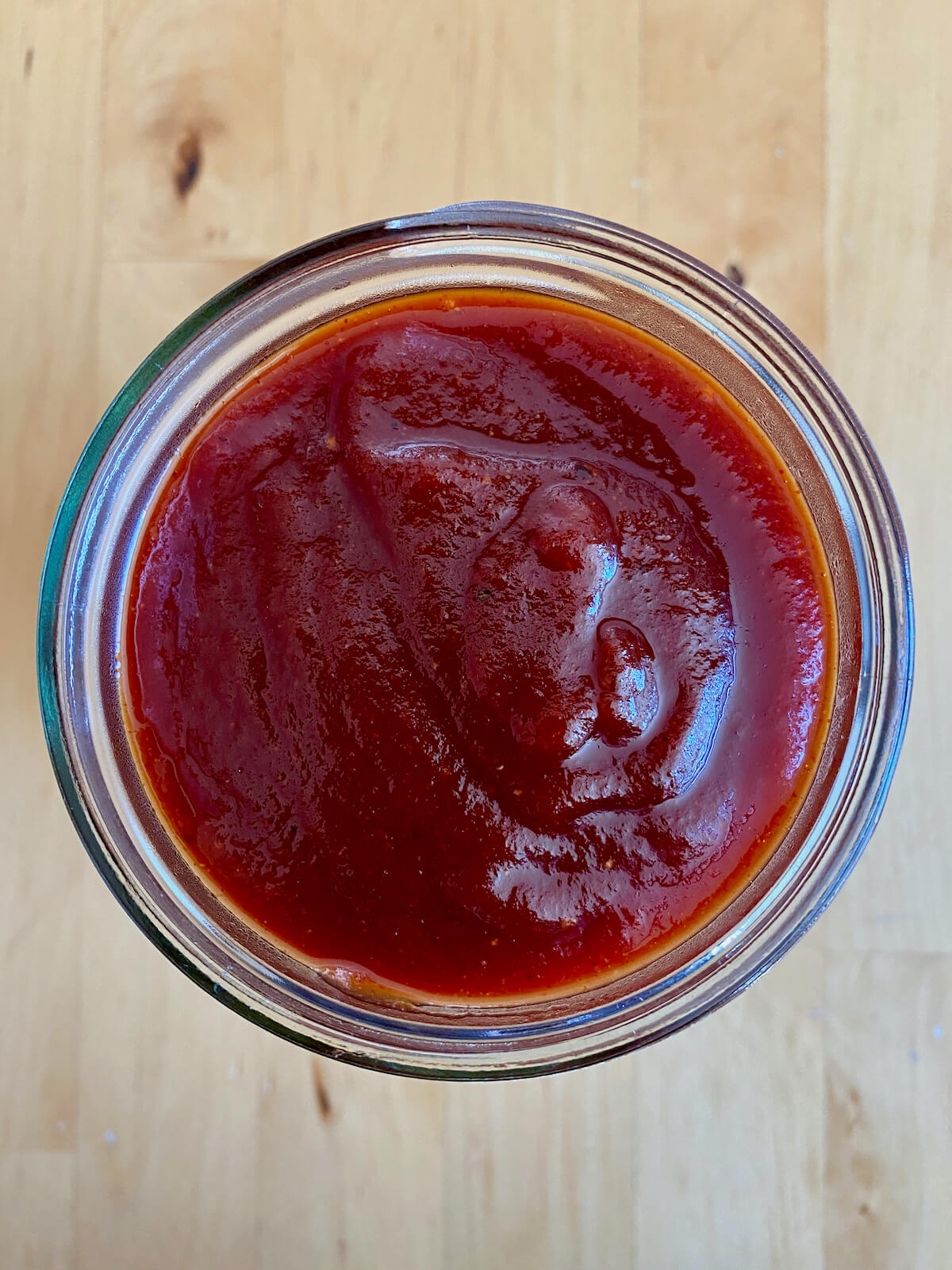 The homemade BBQ sauce in a glass jar on a wooden countertop.