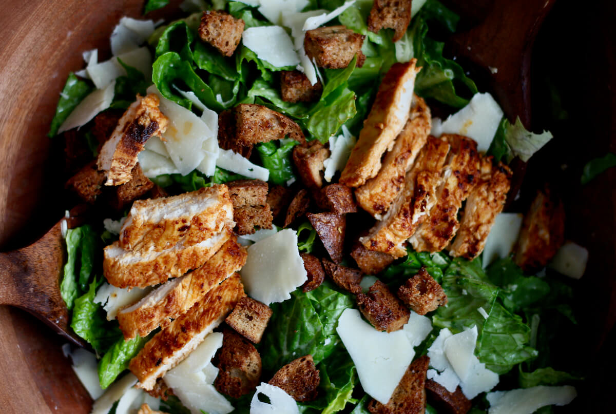 A large wooden salad bowl filled with buffalo chicken caesar salad.