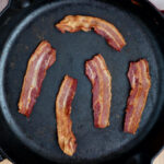 Five strips of bacon in a cast iron skillet.
