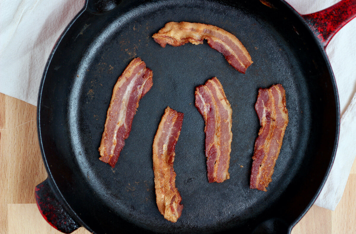 Five strips of cooked bacon in a cast iron skillet.