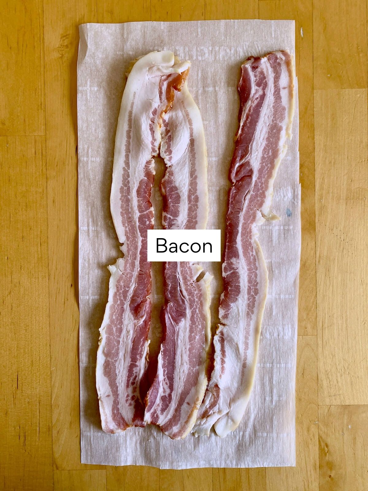Three long strips of raw bacon on a sheet of parchment paper.