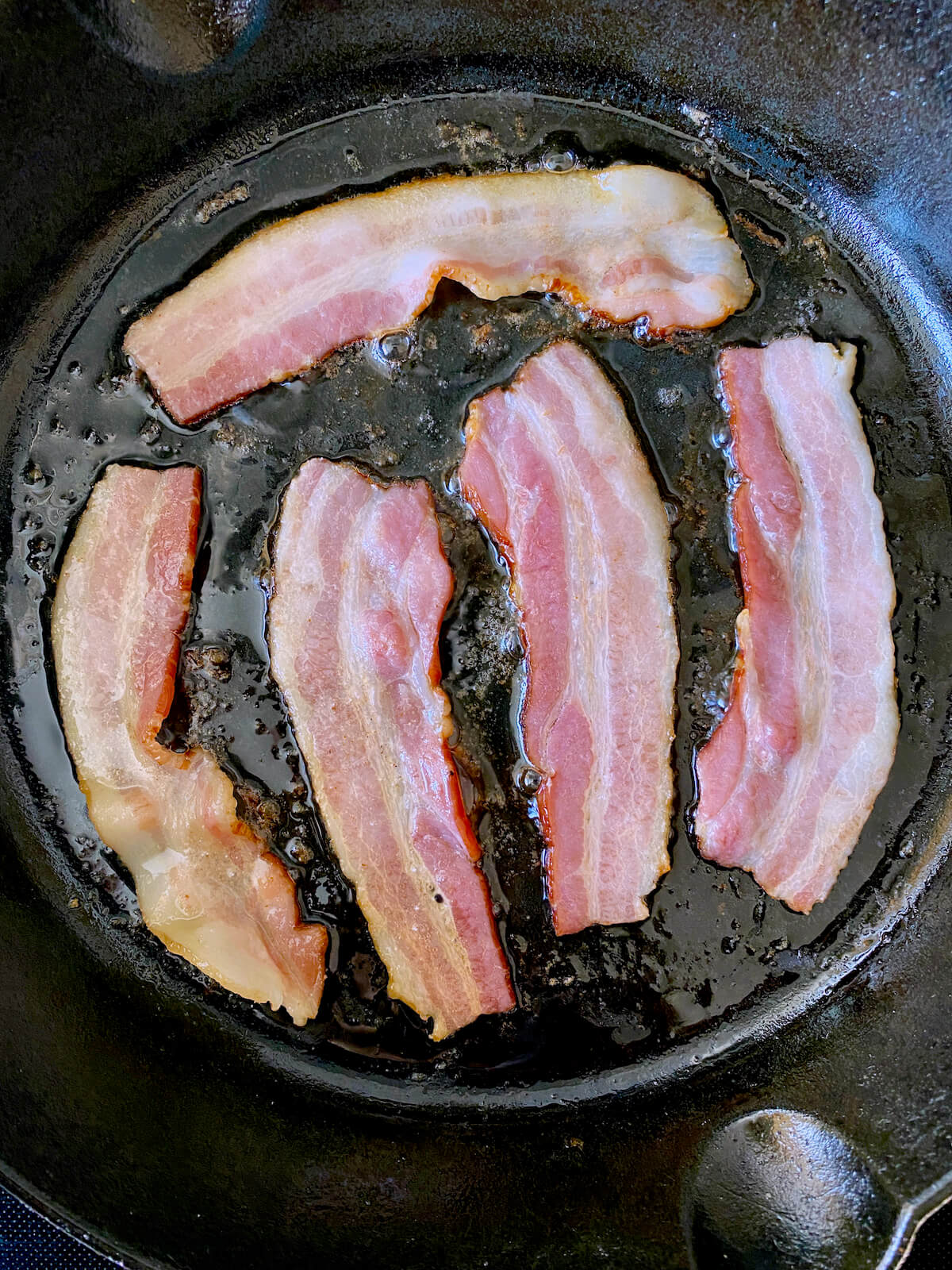 Partially cooked bacon in a cast iron skillet.