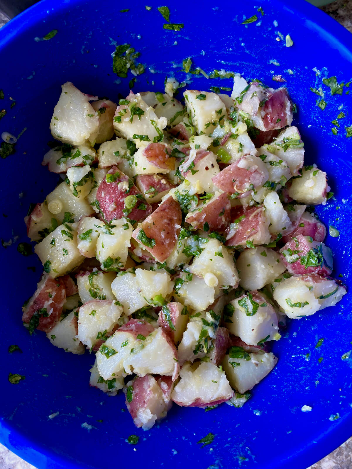 The finished herbed potato salad in a blue mixing bowl.