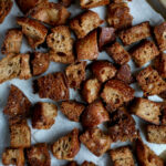 Homemade sourdough croutons on a parchment-lined baking sheet.