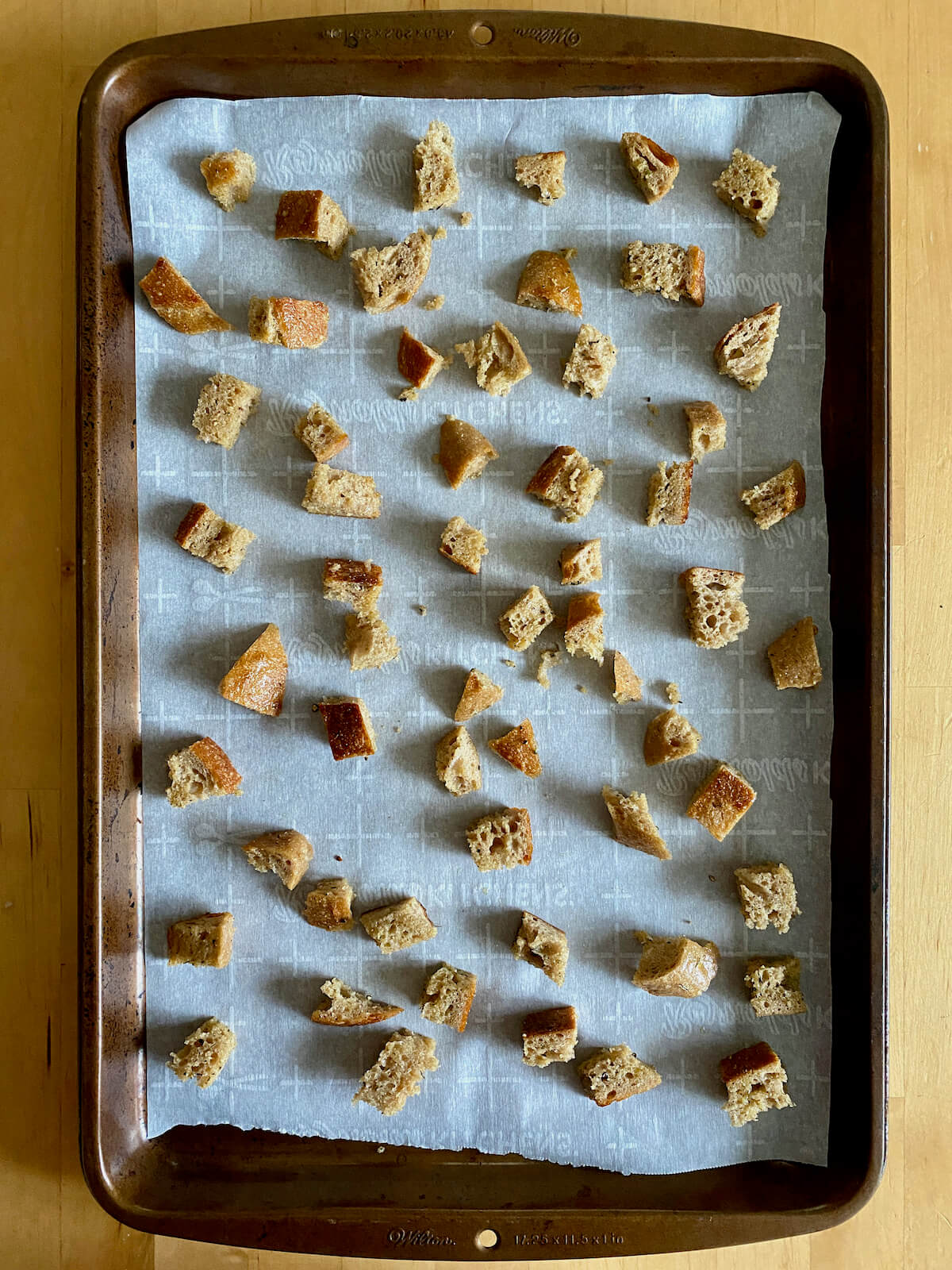 Seasoned sourdough bread cubes spread out on a parchment-lined baking sheet.