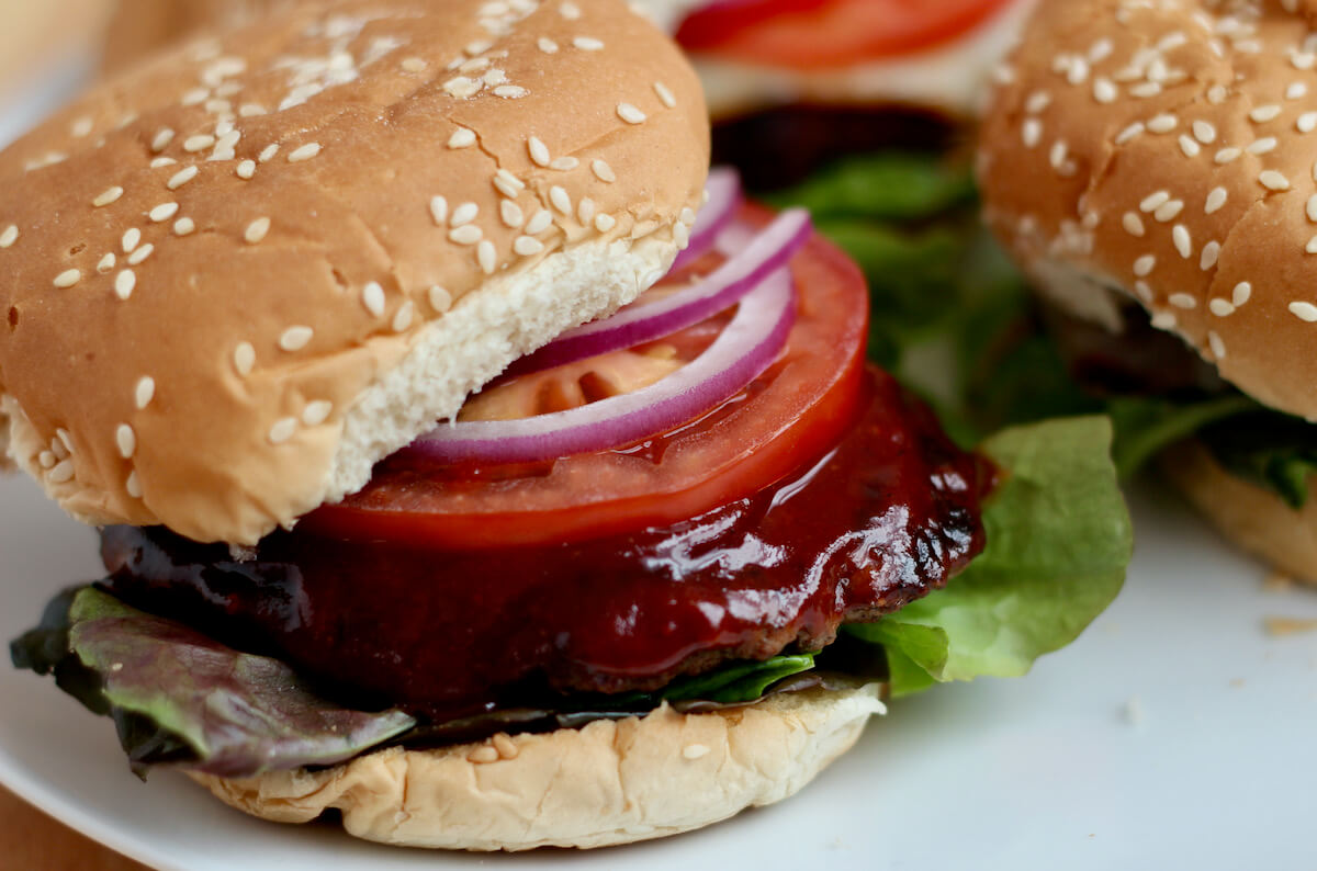 Turkey smash burgers on a plate topped with BBQ sauce, tomato, lettuce, and red onion.