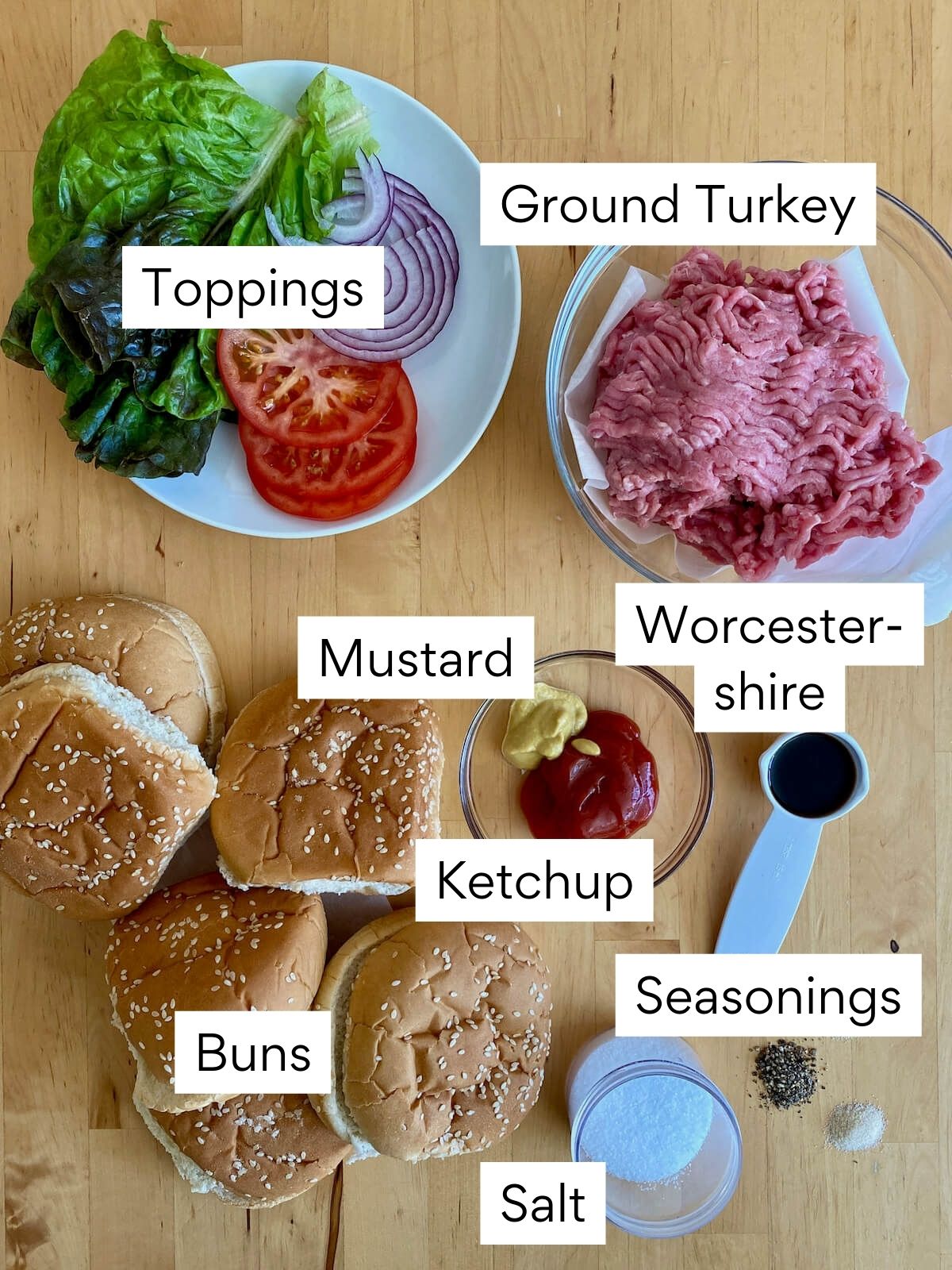 The ingredients to make turkey smash burgers. Each ingredient is labeled with text. They include ground turkey, Worcestershire sauce, mustard, ketchup, seasonings, salt, buns, and toppings.