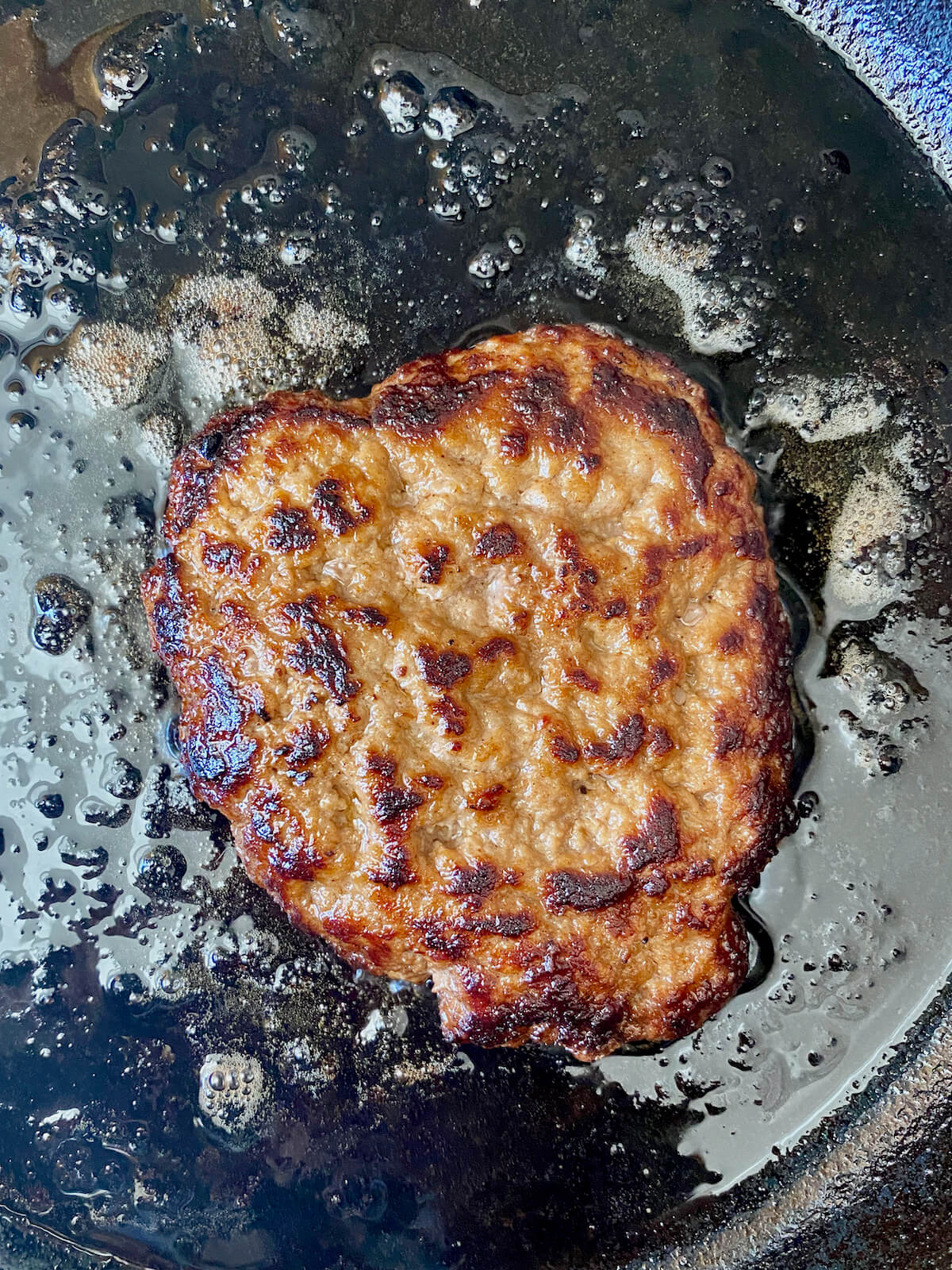 A seared turkey smash burger cooking in a cast iron skillet.