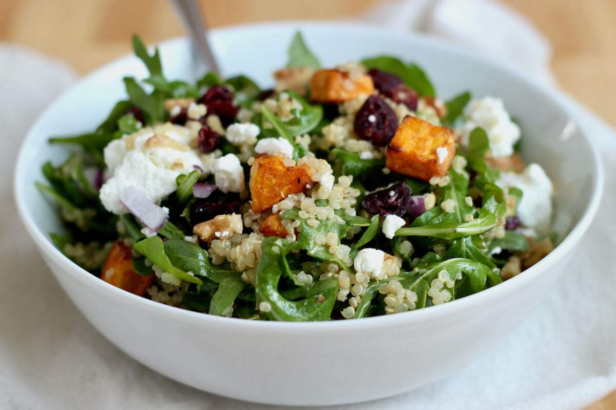 Goat cheese and quinoa arugula salad in a white bowl.