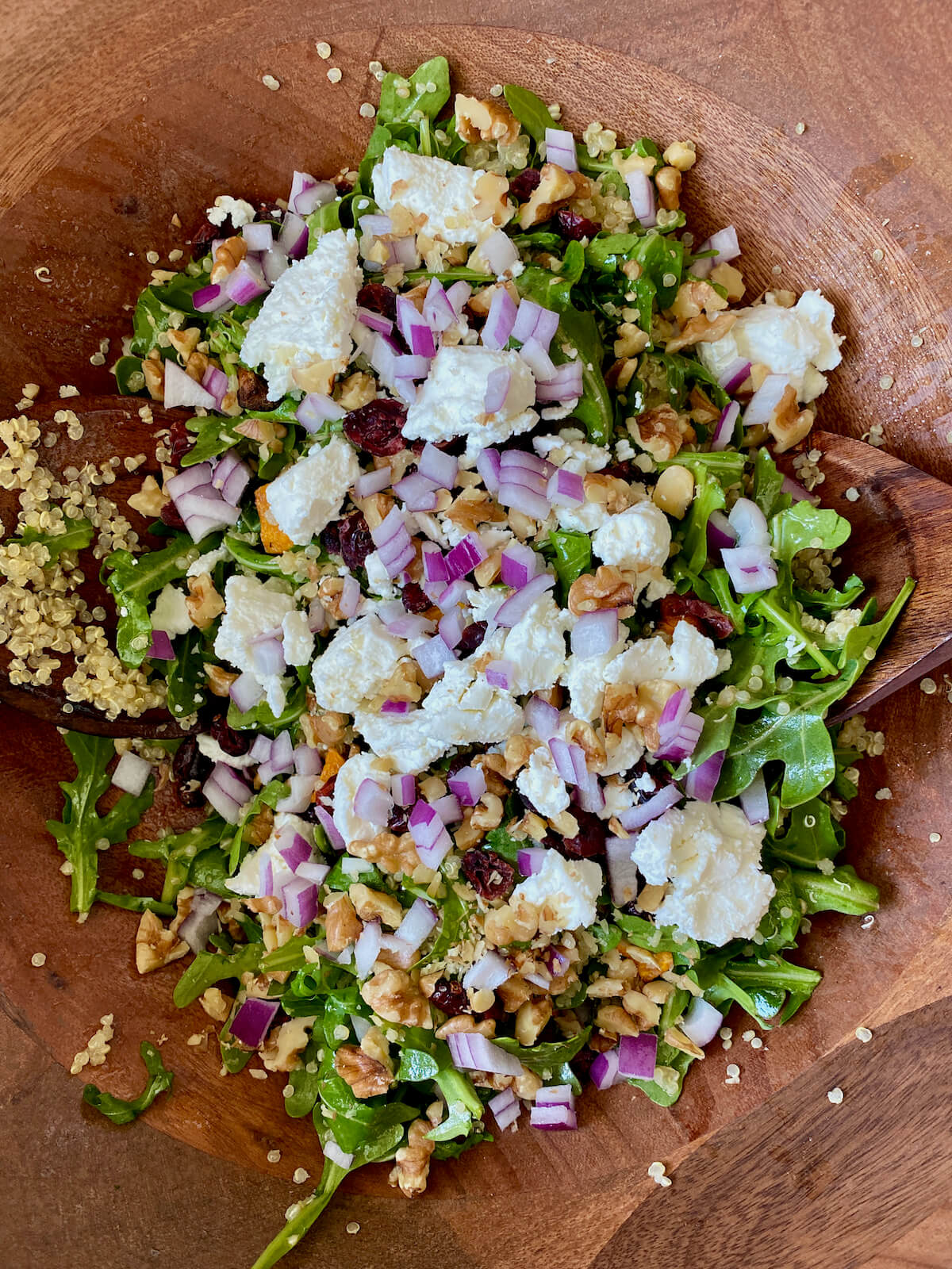 Arugula quinoa salad assembled in a wooden salad bowl.