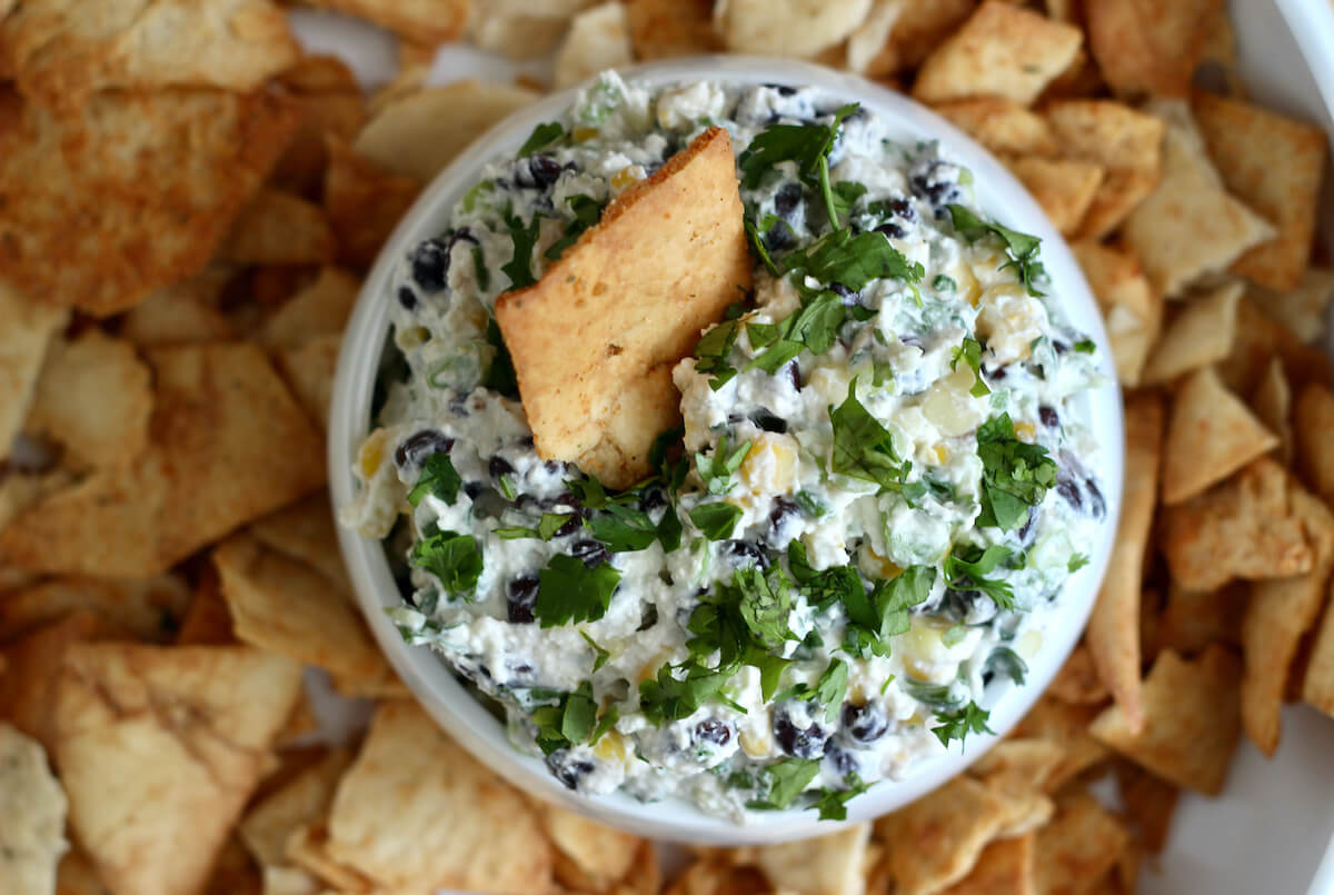 A bowl of black bean corn feta dip surrounded by pita chips.
