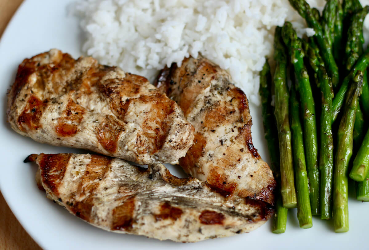 Grilled chicken breast with asparagus and rice on a white dinner plate.