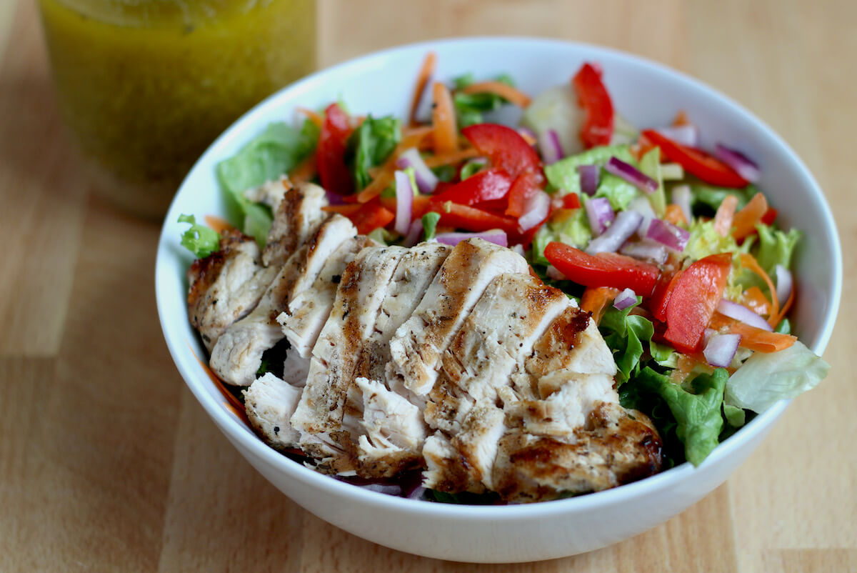 Sliced grilled chicken breast on top of a leafy green salad.