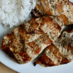 Three grilled chicken breasts on a dinner plate next to a serving of rice.
