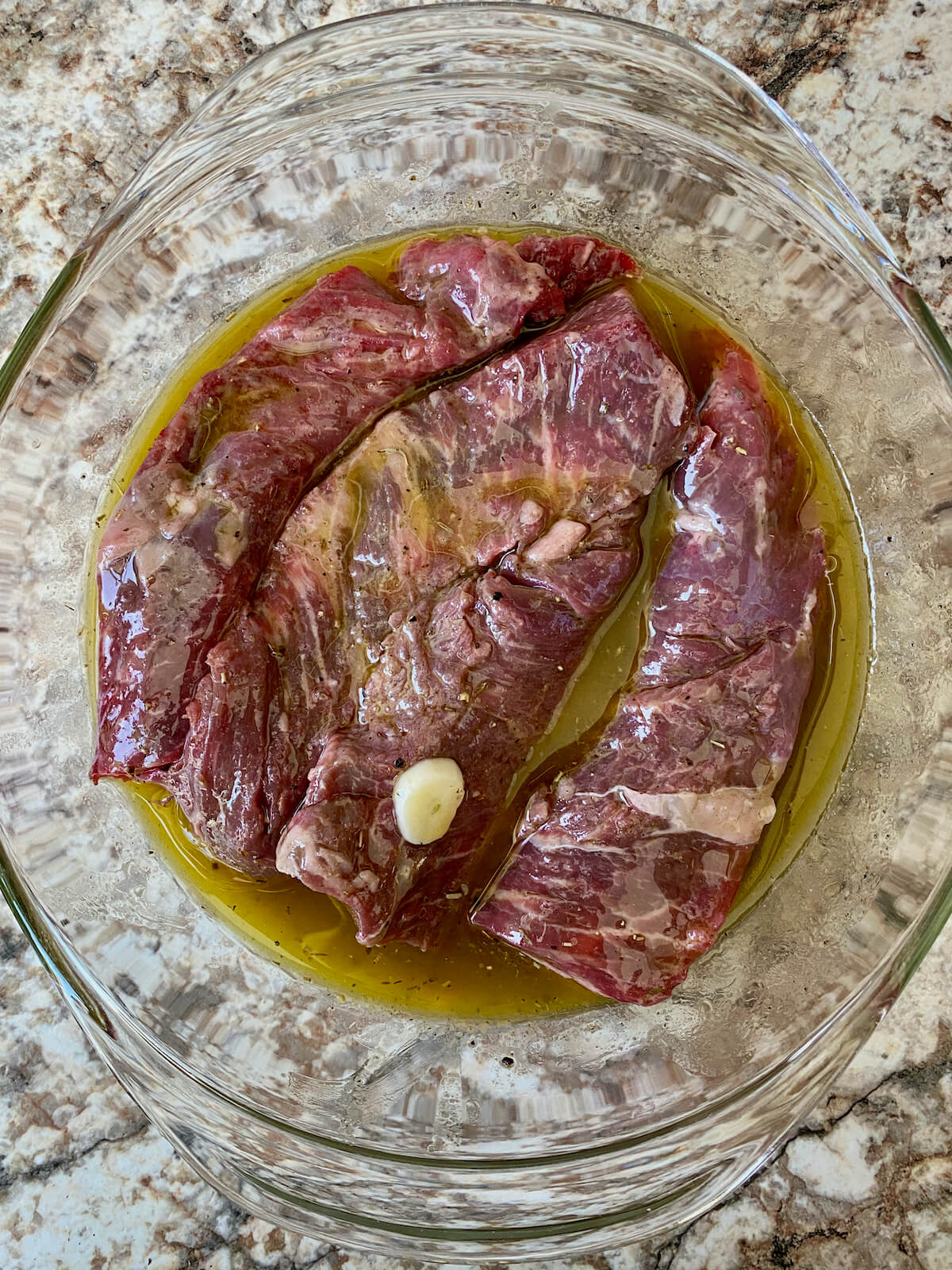Raw strips of sirloin steak marinating in a red wine vinaigrette in a glass bowl.