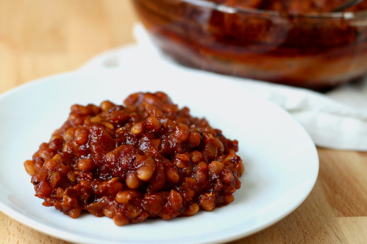 A plateful of honey baked beans next to the casserole dish.