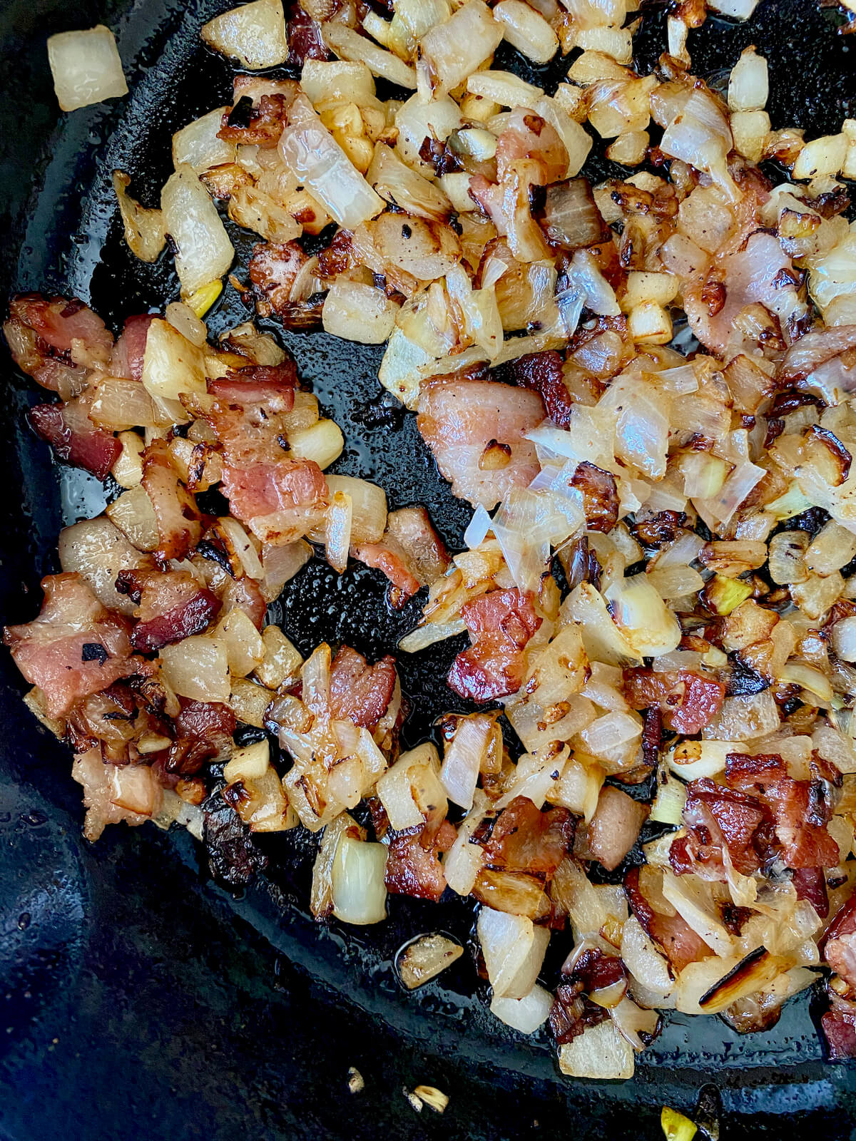 Chopped bacon, onion, and garlic sautéing in a cast iron skillet.