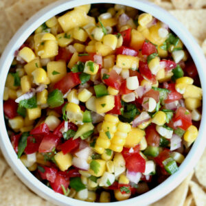 A small white bowl filled with mango corn salsa surrounded by tortilla chips.