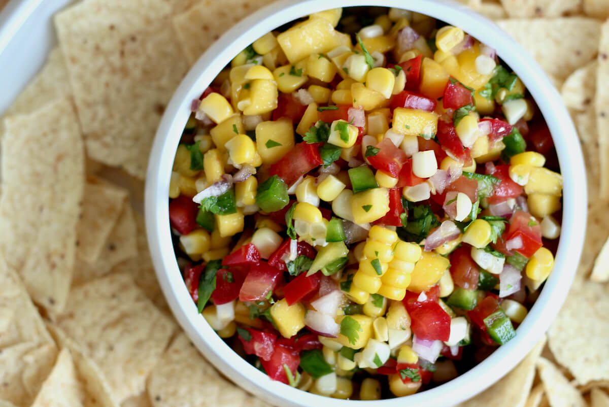 A bowl of mango corn salsa inside a larger serving bowl filled with tortilla chips.