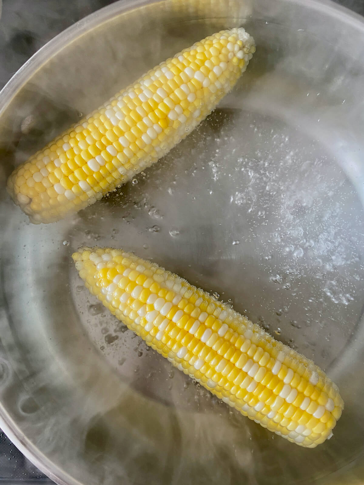 Two ears of corn cooking in a boiling pot of water.