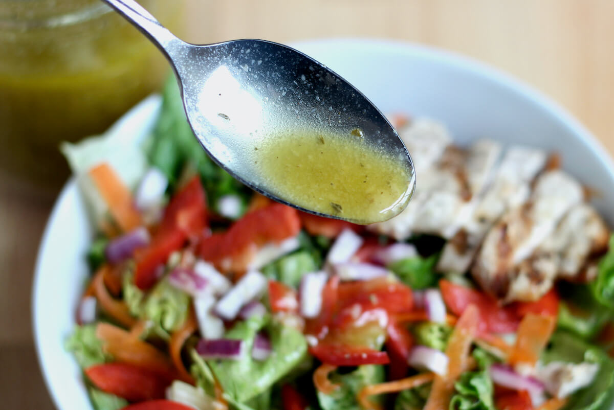 A spoon drizzling red wine vinaigrette dressing over a bowl of salad.