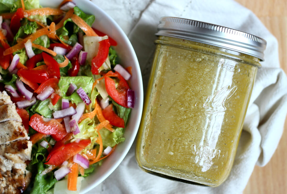 A jar of red wine vinegar salad dressing next to a salad with grilled chicken.