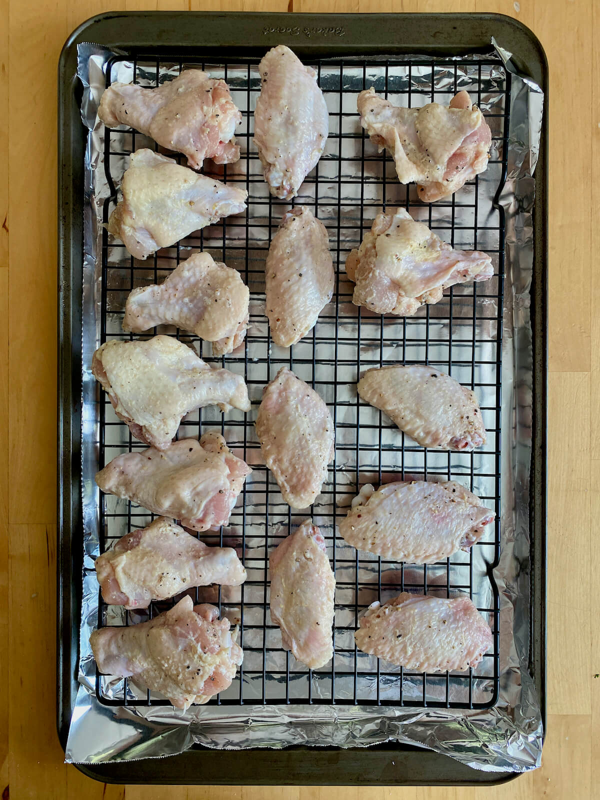 Raw chicken wings spread out on a wire rack set on top of a foil-lined baking sheet.