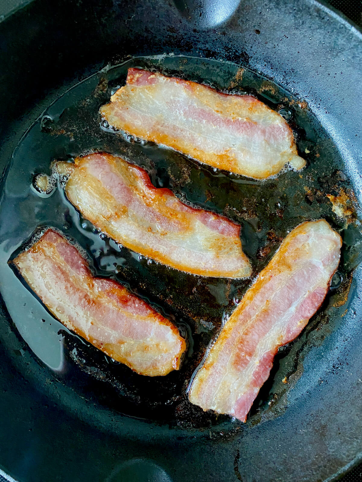 Bacon cooking in a cast iron skillet.