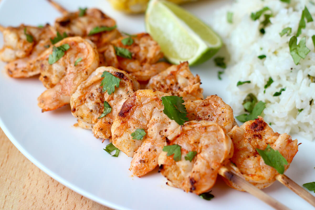 Two skewers of Old Bay grilled shrimp served with rice and corn on the cob.