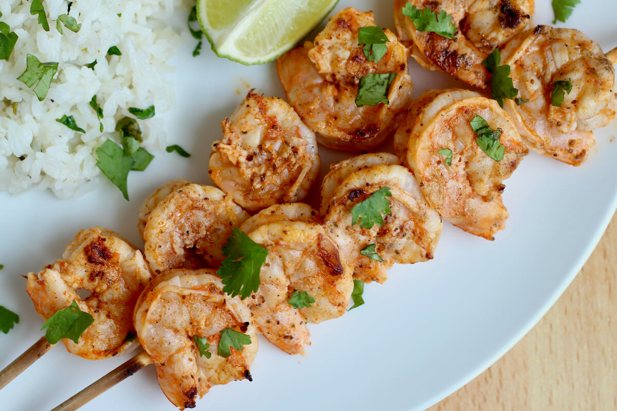Two skewers of Old Bay grilled shrimp on a white plate.