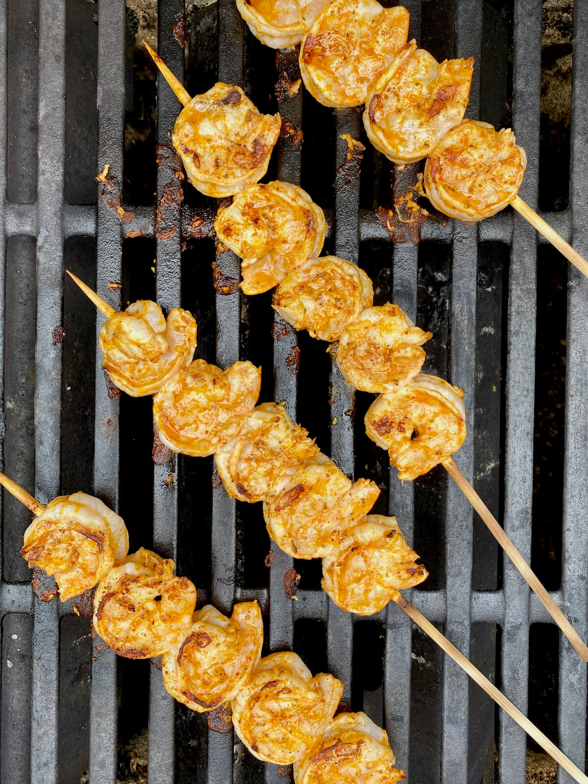 Four skewers of shrimp cooking on the grill.