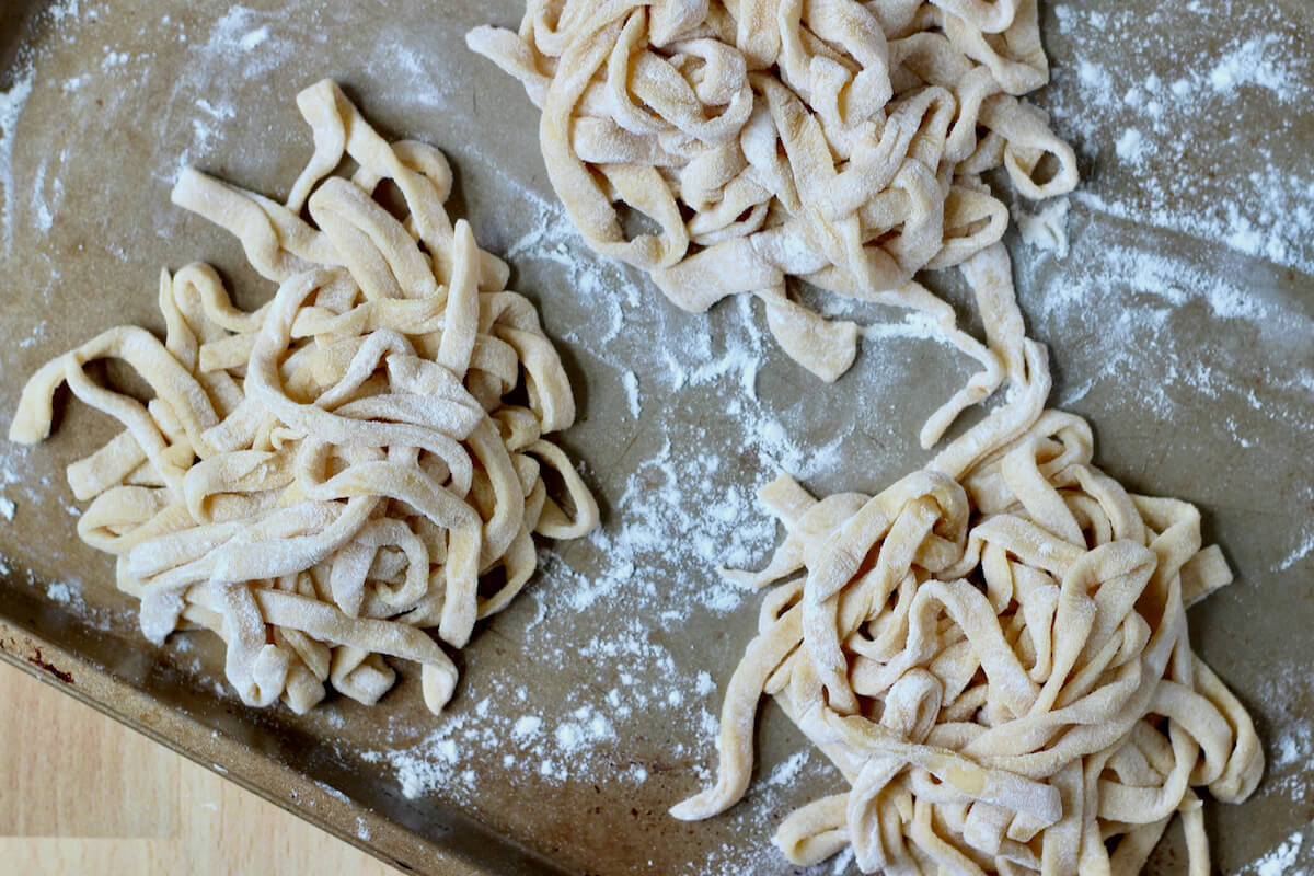 Three nests of homemade sourdough pasta noodles on a flour-dusted baking sheet.