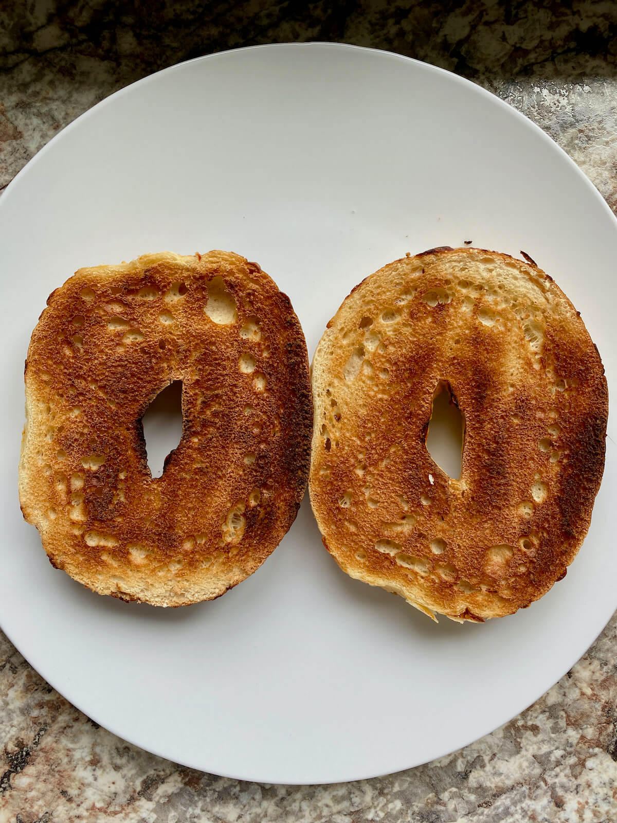 Two halves of a toasted bagel on a white plate.