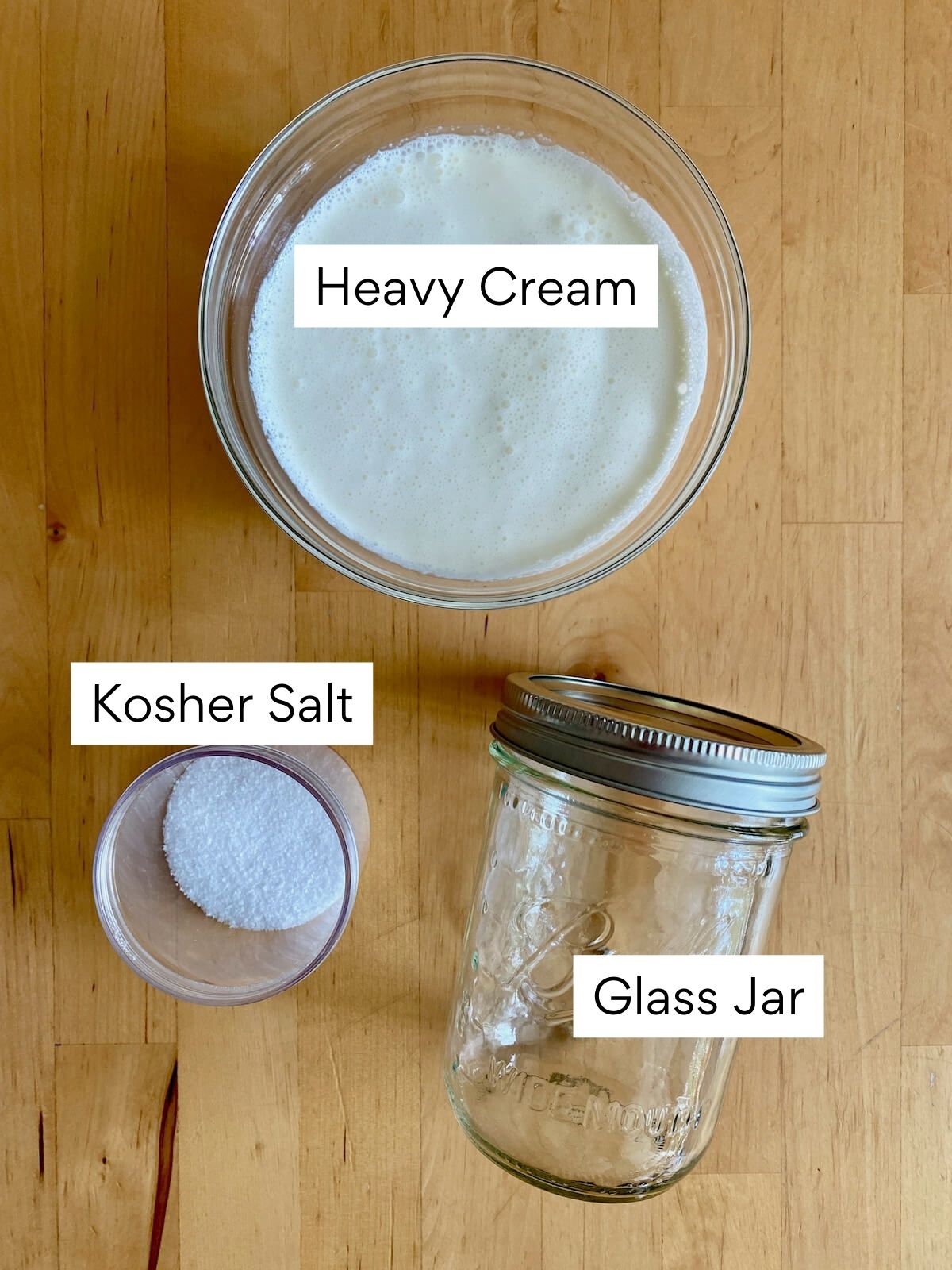 The ingredients to make homemade butter in a jar. Each ingredient is labeled with text. They include heavy cream, kosher salt, and a glass jar.