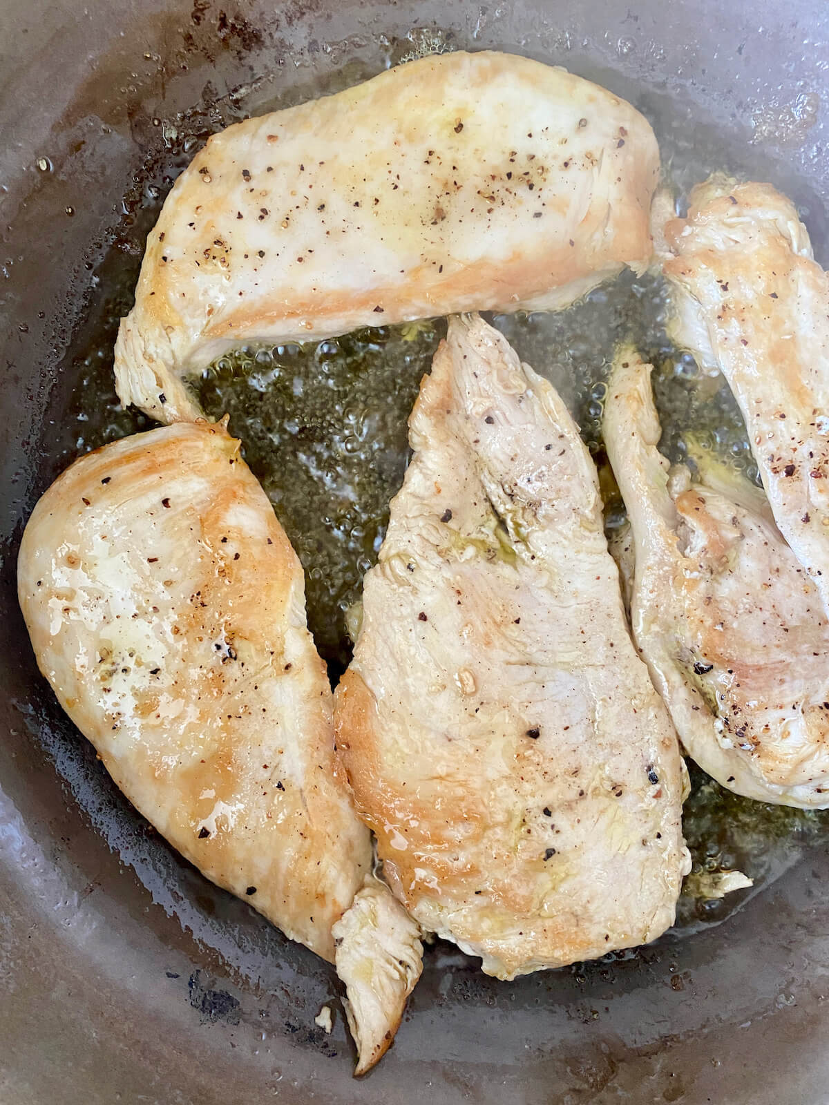 Four chicken breasts searing in olive oil in a Dutch oven.