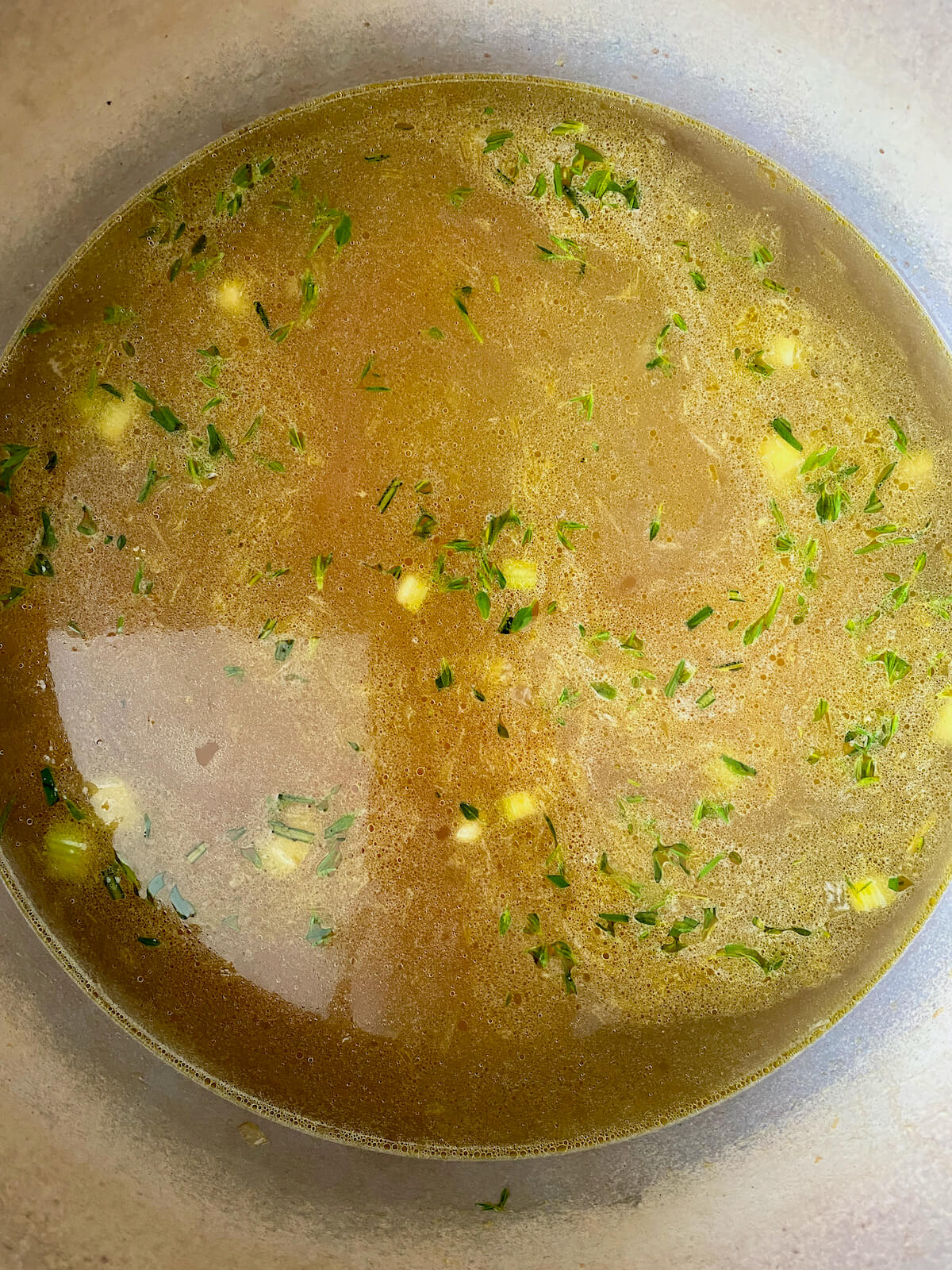 Chicken stock, vegetables, and herbs simmering in a Dutch oven.