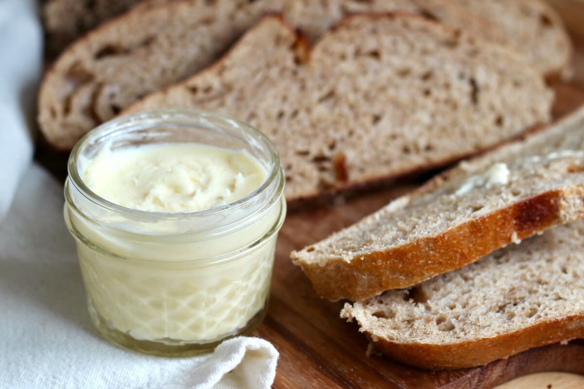A jar of butter sitting next to slices of sourdough bread on a wooden cutting board.